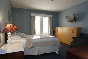 A hotel room with a bed, bedside lamps, a TV mounted on the wall, a wooden dresser, and a window with curtains. - Irving House At Harvard (Cambridge)