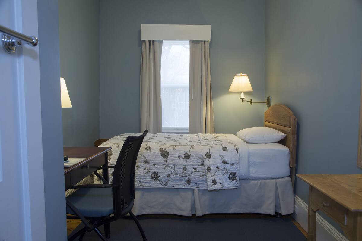 Habitación de hotel con cama, escritorio, silla y ventana con cortinas.
