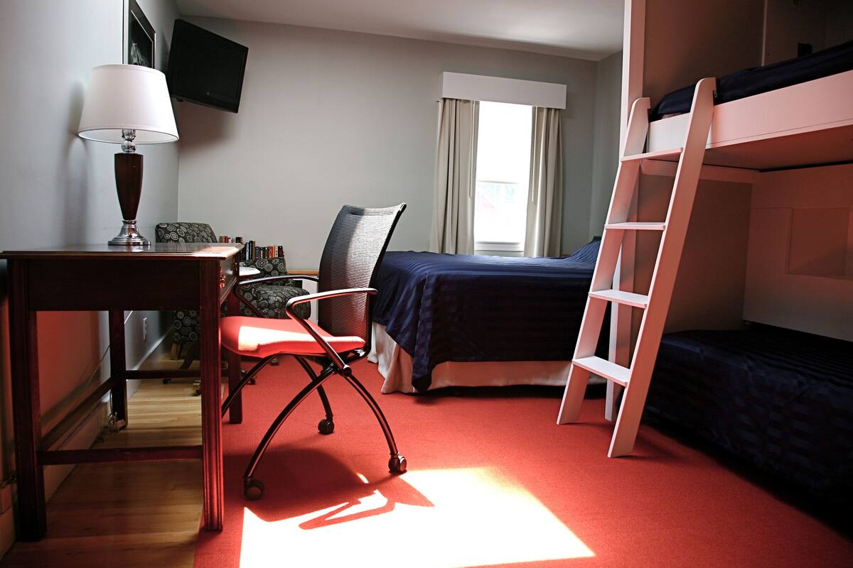 Una habitación con una litera, un escritorio con lámpara, una silla y un ventanal con cortinas.