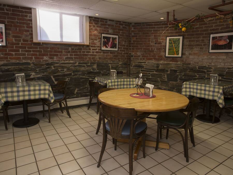Un restaurant aux murs de briques, au sol carrelé et aux nappes à carreaux. Les tables sont entourées de chaises.