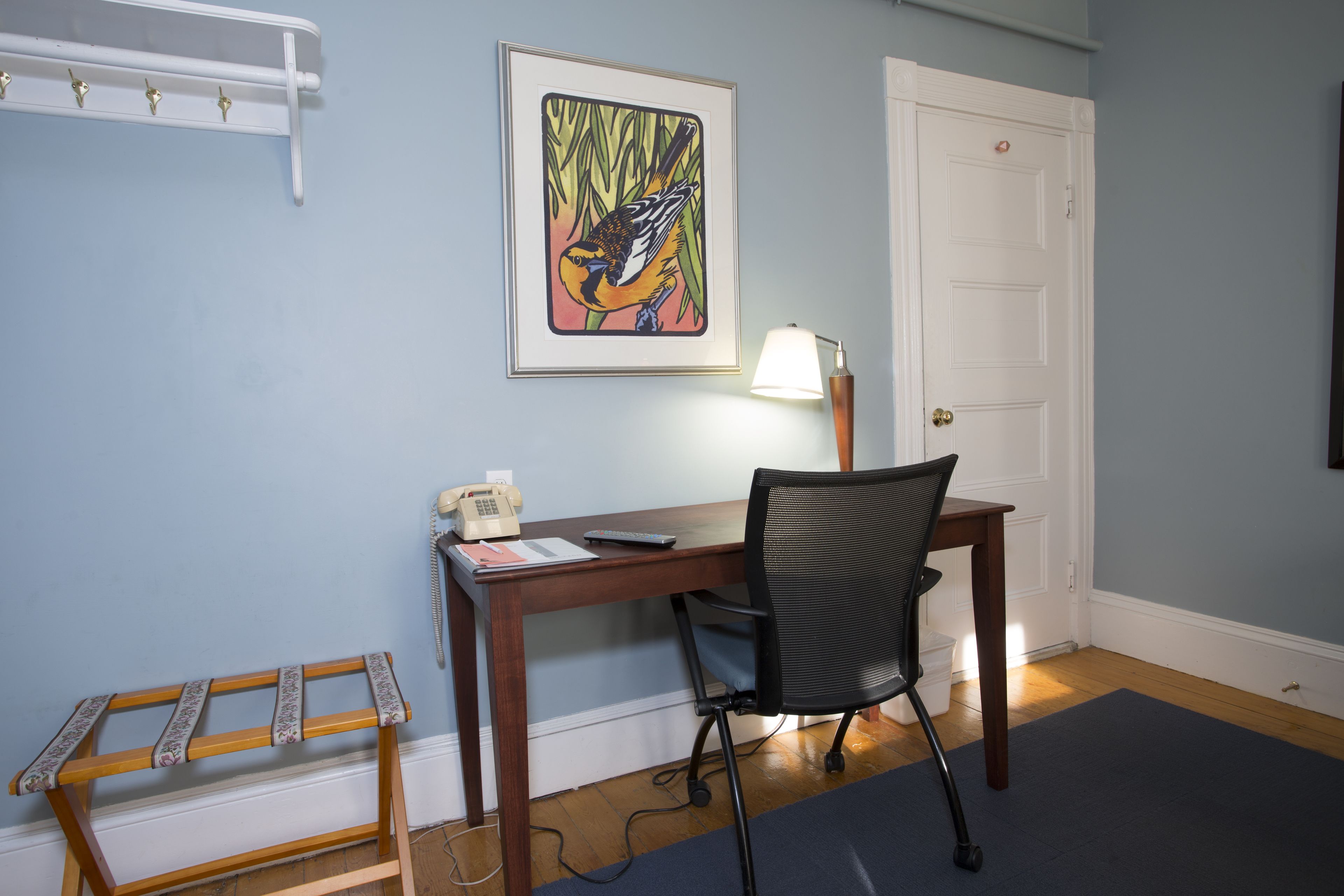 A room with a wooden desk, a black office chair, a telephone, and a framed artwork on the wall.