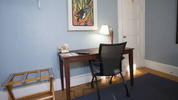 A room with a wooden desk, a black office chair, a telephone, and a framed artwork on the wall.
