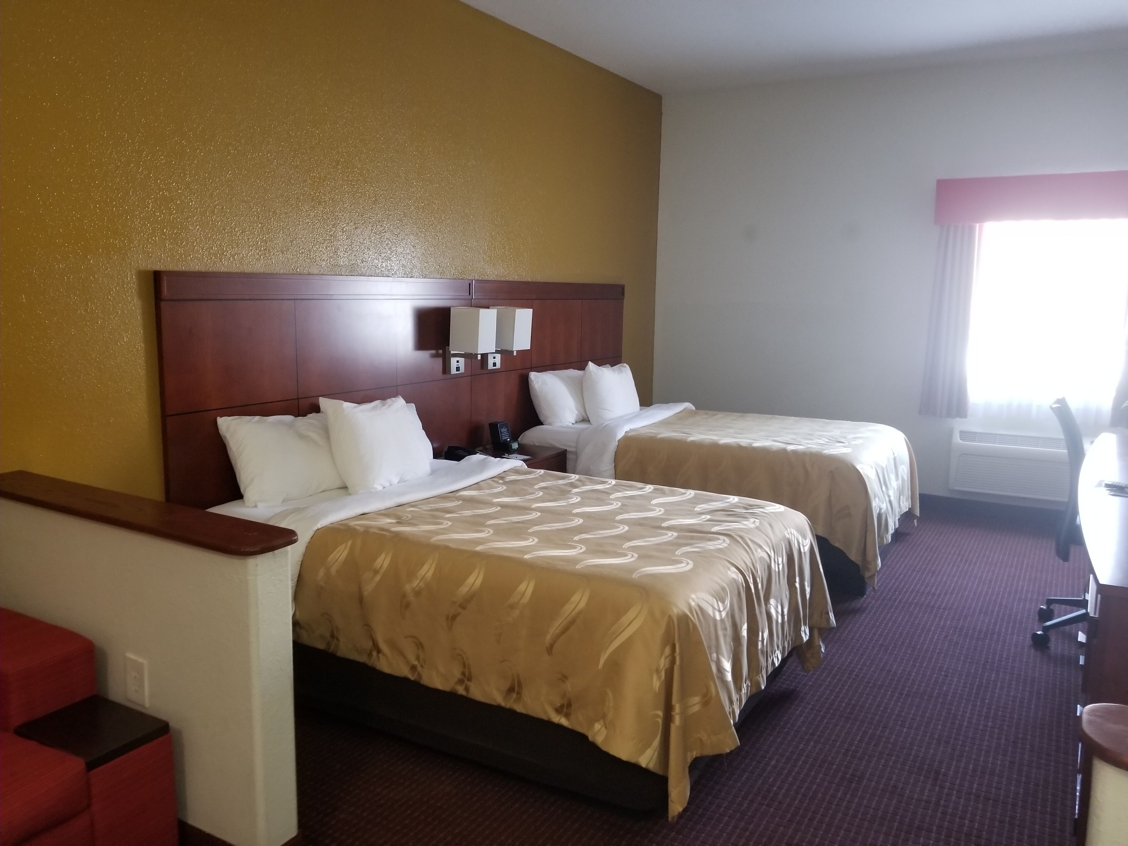 A hotel room with two beds, a wooden headboard, a desk, and a chair.