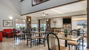 A spacious dining area with multiple tables and chairs, a red sofa, and a television mounted on the wall. - Quality Inn Zephyrhills-dade City (Zephyrhills)