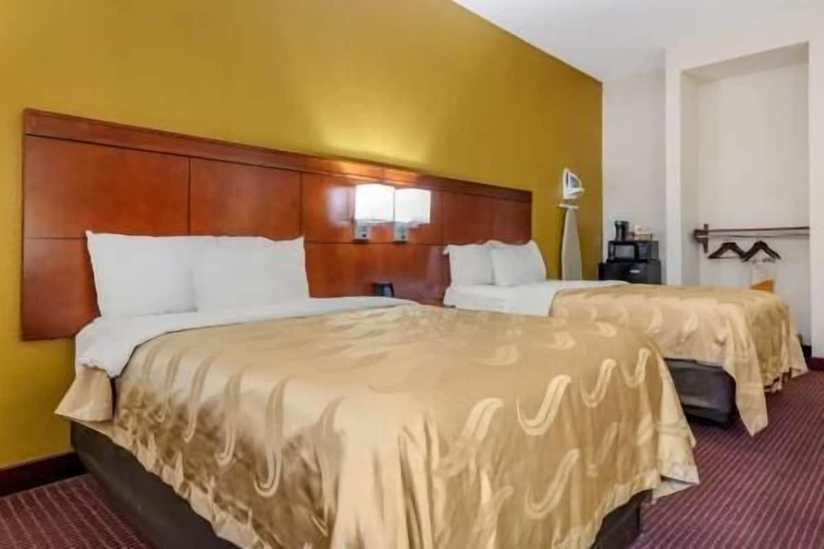 A hotel room with two beds, a wooden headboard, a bedside table, and a lamp.