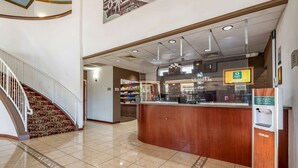 A hotel lobby with a reception desk, a staircase, and a view of the kitchen area. - Quality Inn Zephyrhills-dade City (Zephyrhills)