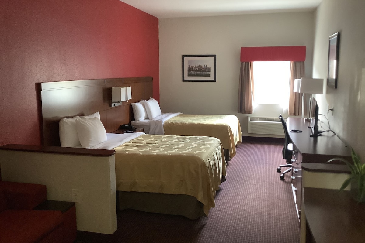 A hotel room with two beds, a desk, a chair, a TV, and a window with curtains.