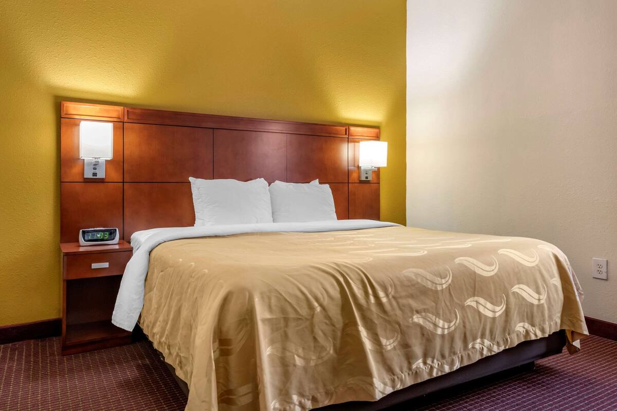 A hotel room with a bed, nightstands, and wall-mounted lamps.