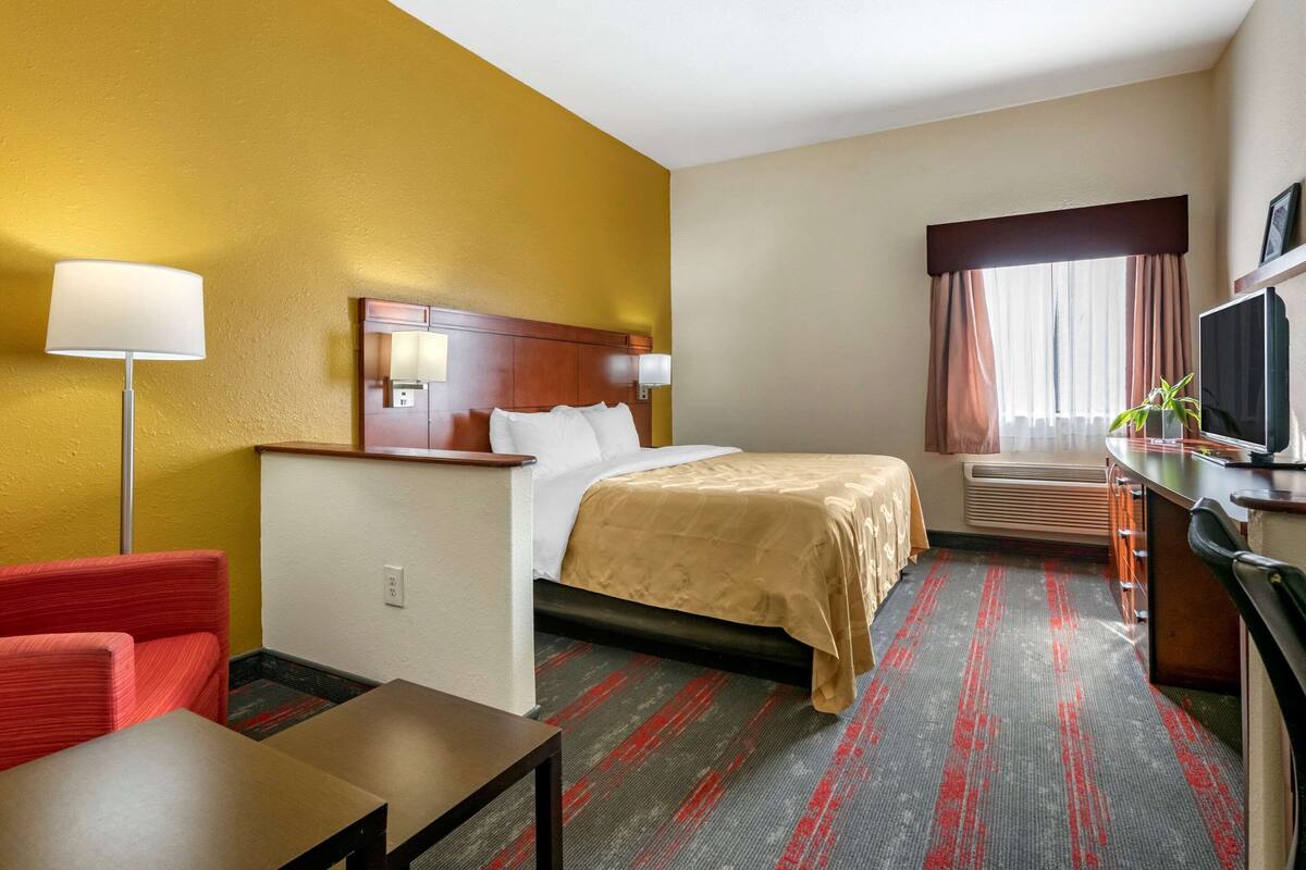 A hotel room with a bed, a desk, a chair, a TV, and a window with curtains.