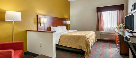 A hotel room with a bed, a desk, a chair, a TV, and a window with curtains.
