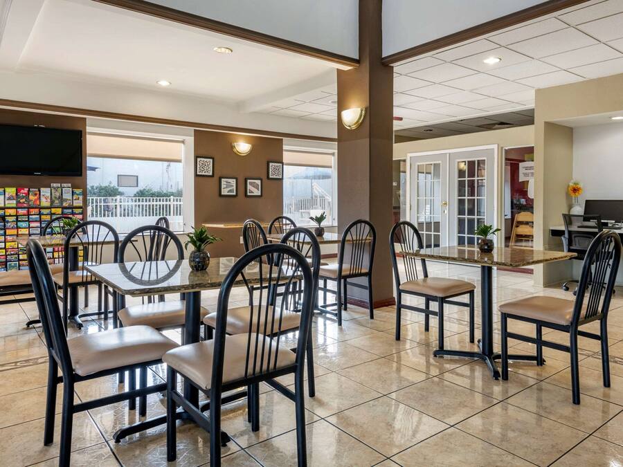 A spacious dining area with multiple tables and chairs, a television mounted on the wall, and a view of the outdoors through large windows.