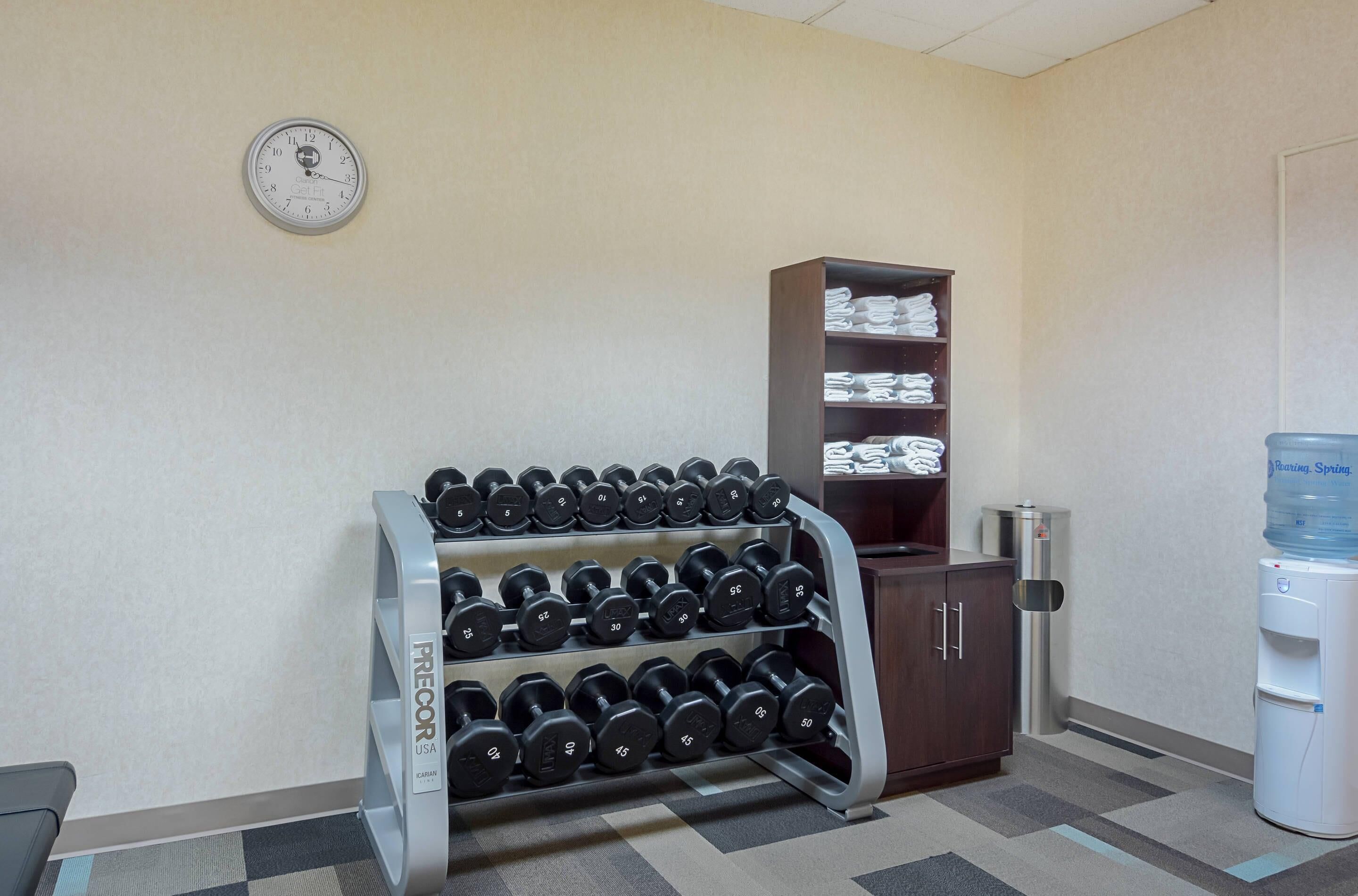A gym area with a dumbbell rack, a clock, a water dispenser, and a cabinet with folded towels.