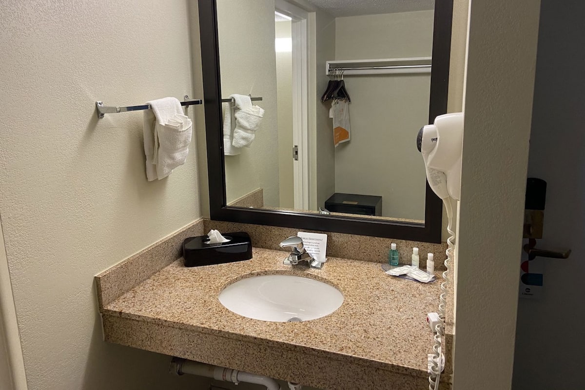 A bathroom with a granite countertop, a white sink, a mirror, a towel rack, a hairdryer, and toiletries.