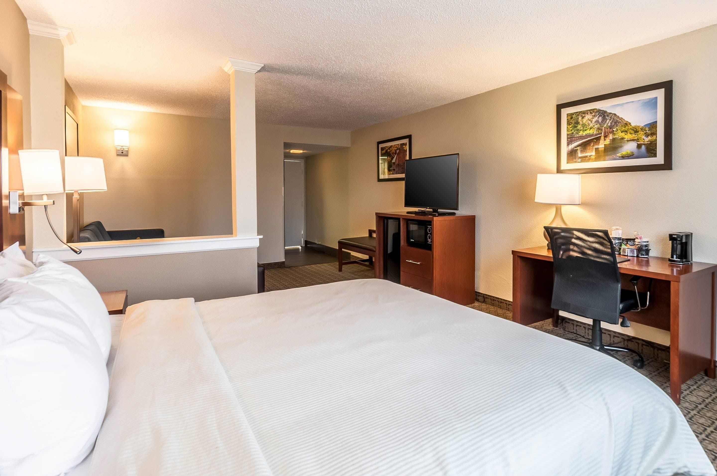 A hotel room with a large bed, a desk with a chair, a television, and a desk lamp.