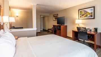 A hotel room with a large bed, a desk with a chair, a television, and a desk lamp.