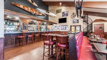 A bar area with wooden bar stools, a counter with bottles, and a staircase leading to an upper level.