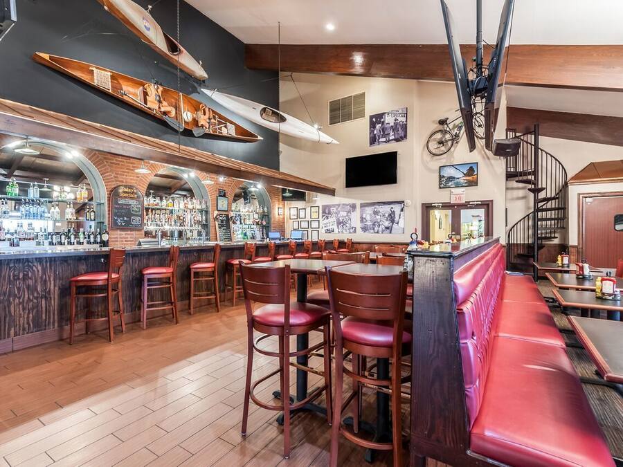 A bar area with wooden bar stools, a counter with bottles, and a staircase leading to an upper level.
