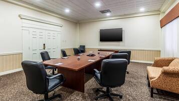 A conference room with a long table, six black office chairs, a television on the wall, and a patterned carpet.