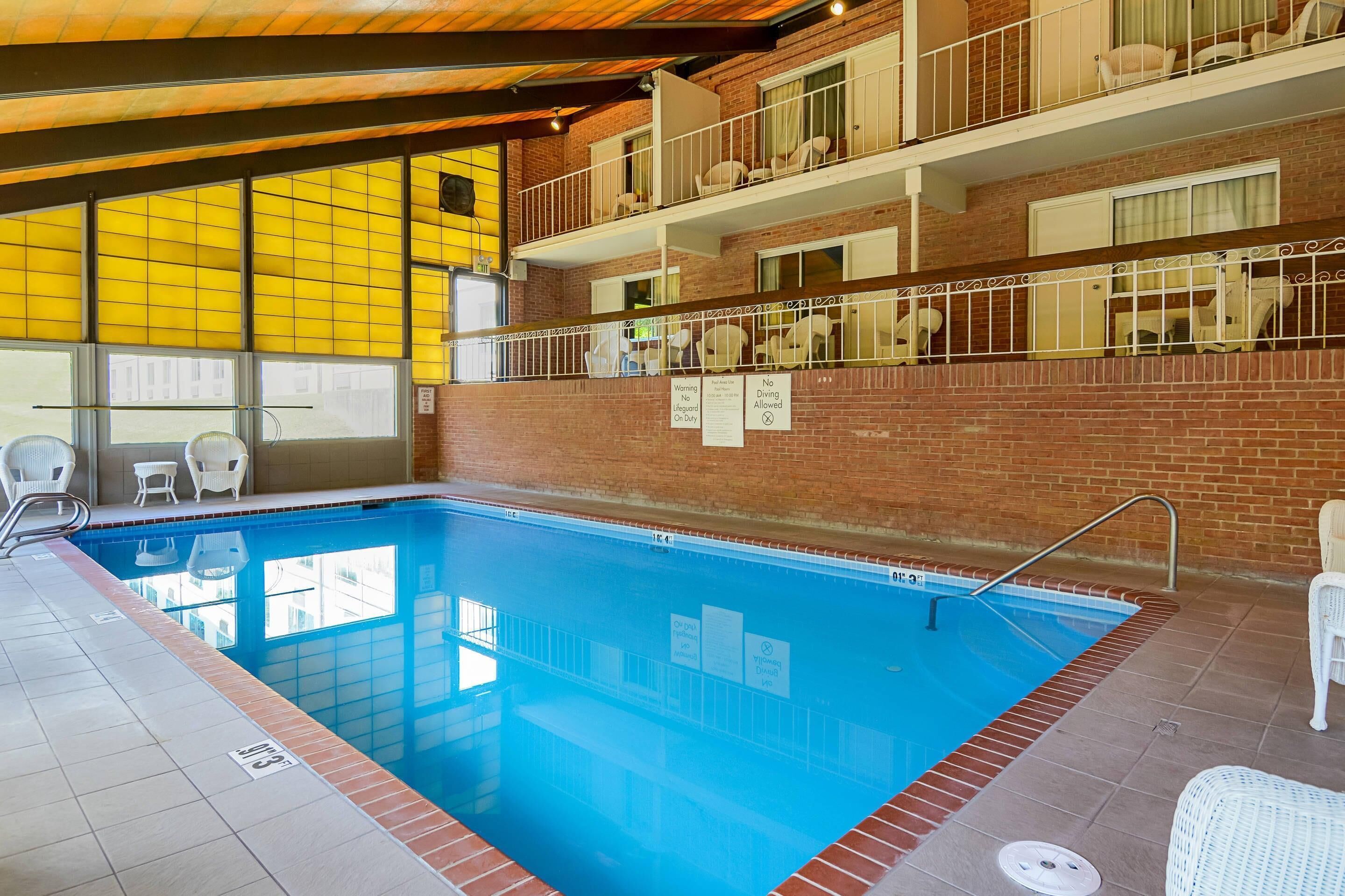 Una piscina interior con agua cristalina azul, rodeada por un muro de ladrillo y barandillas blancas.