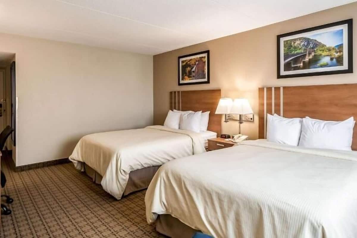 A hotel room with two beds, a desk, a chair, and two framed pictures on the wall.