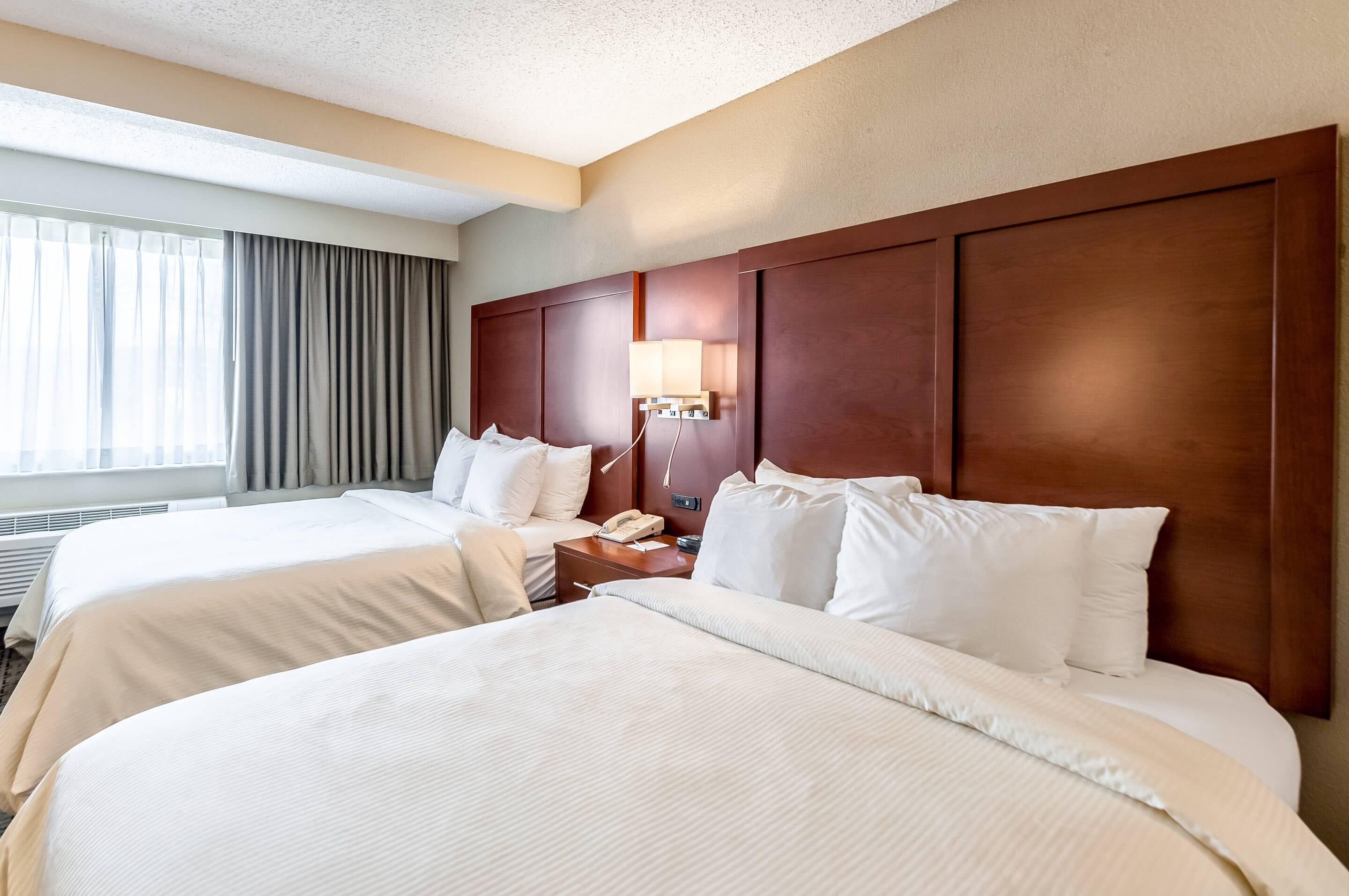 A hotel room with two beds, a nightstand with a lamp, and a window with curtains.
