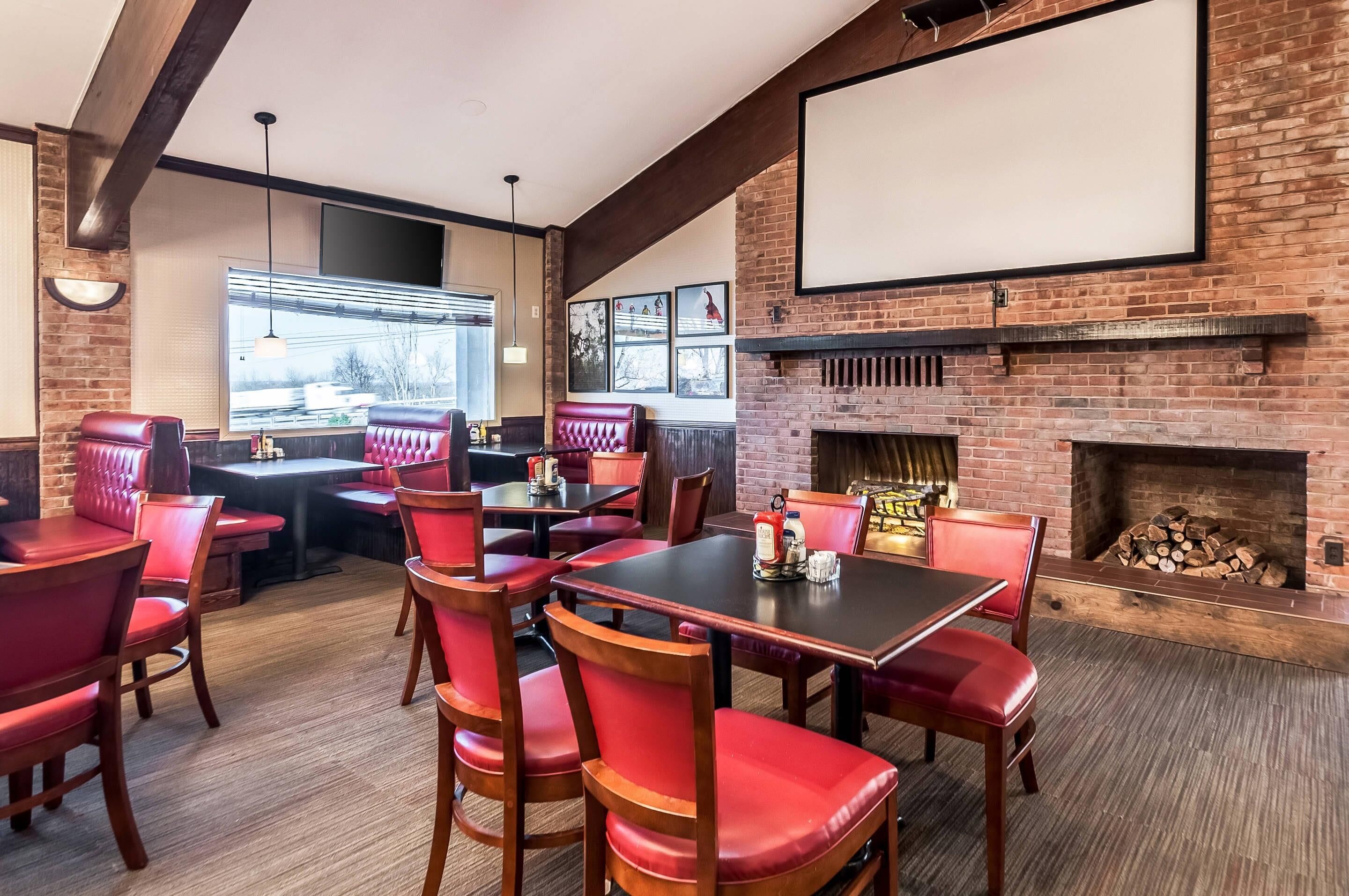 A restaurant with red leather booths and tables, a brick fireplace, and a large screen on the wall.