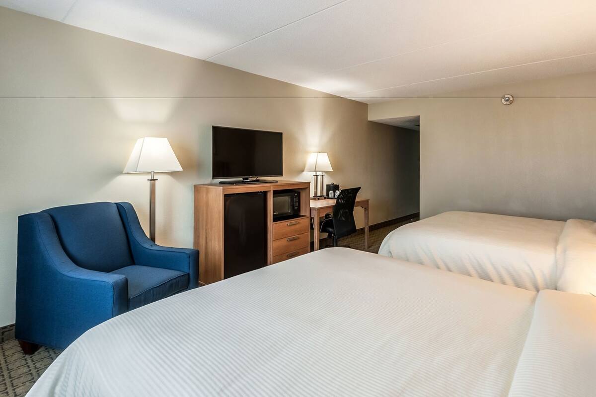 Habitación de hotel con dos camas, un escritorio, un televisor, una silla y dos lámparas.