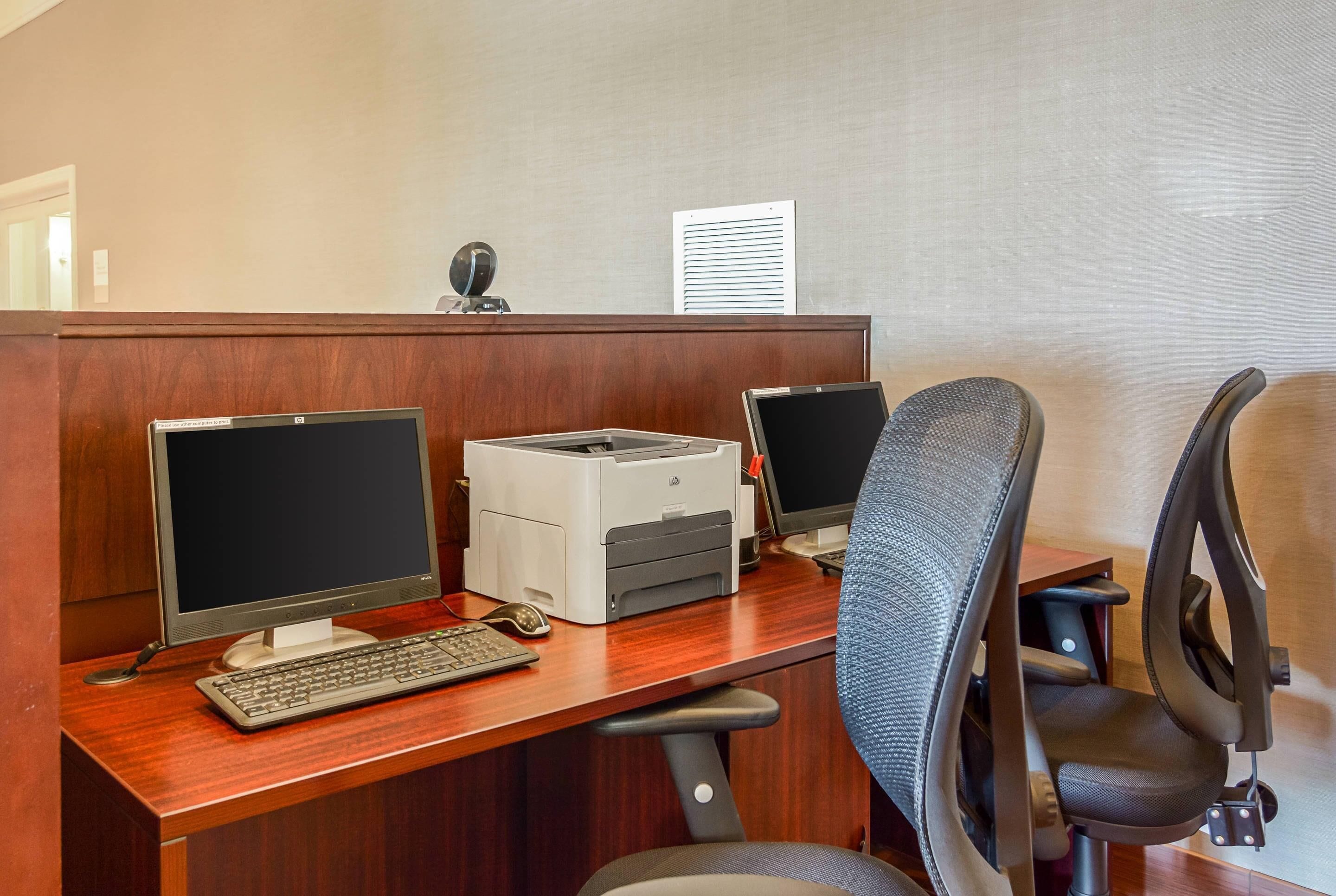 A cubicle with two monitors, a keyboard, a printer, and a chair.