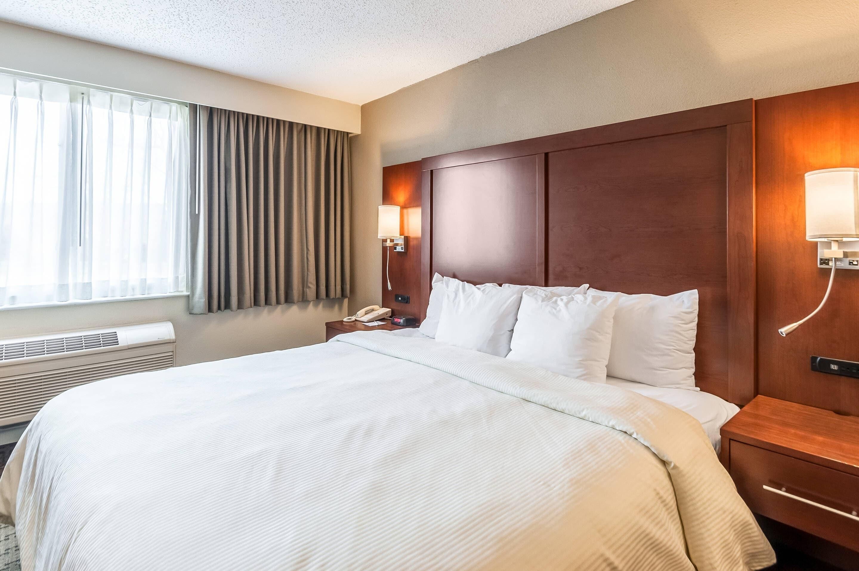 A hotel room with a large bed, a bedside table with a lamp, a phone, and a wall-mounted light.