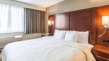 A hotel room with a large bed, a bedside table with a lamp, a phone, and a wall-mounted light.