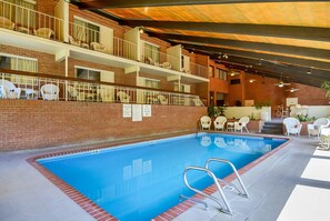 Une piscine intérieure avec un mur en briques, des chaises blanches et un balcon doté de balustrades.