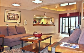A lobby with a sofa, coffee table, and a bowl on the table. There is a clock on the wall and an exit sign.