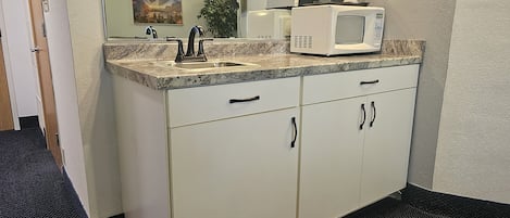 A kitchen with a microwave, stove, and sink. There is a painting on the wall and a plant in the corner.