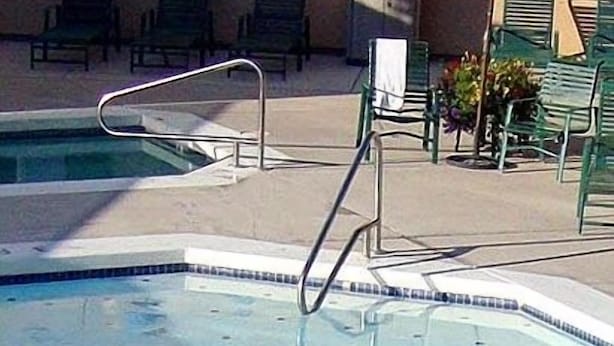 A swimming pool with a clear blue water, surrounded by green lounge chairs and a tiled deck.
