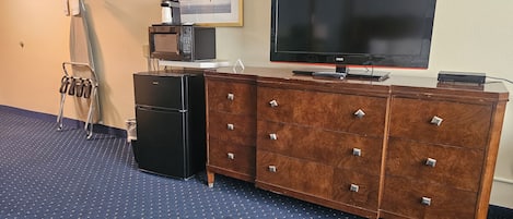 A room with a wooden dresser, a television, a microwave, and a clothes rack.