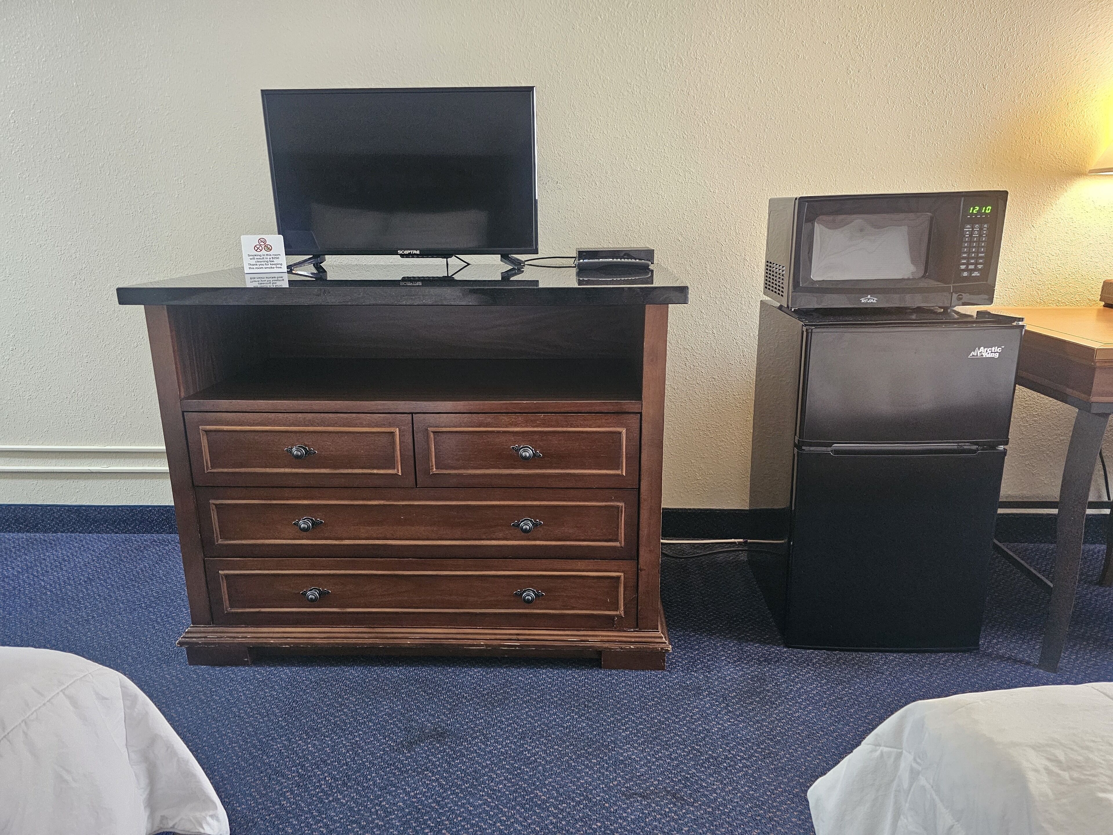 A wooden dresser with a flat-screen TV on top, a microwave, and a refrigerator in a hotel room.