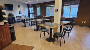 A restaurant interior with multiple tables and chairs, a wooden floor, and large windows.