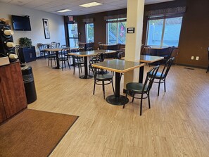 A restaurant interior with multiple tables and chairs, a wooden floor, and large windows.