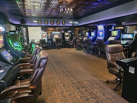 A gaming arcade with multiple gaming machines, leather chairs, and a patterned carpet.
