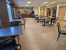 A spacious cafeteria with multiple tables and chairs, a coffee machine, and a counter area.