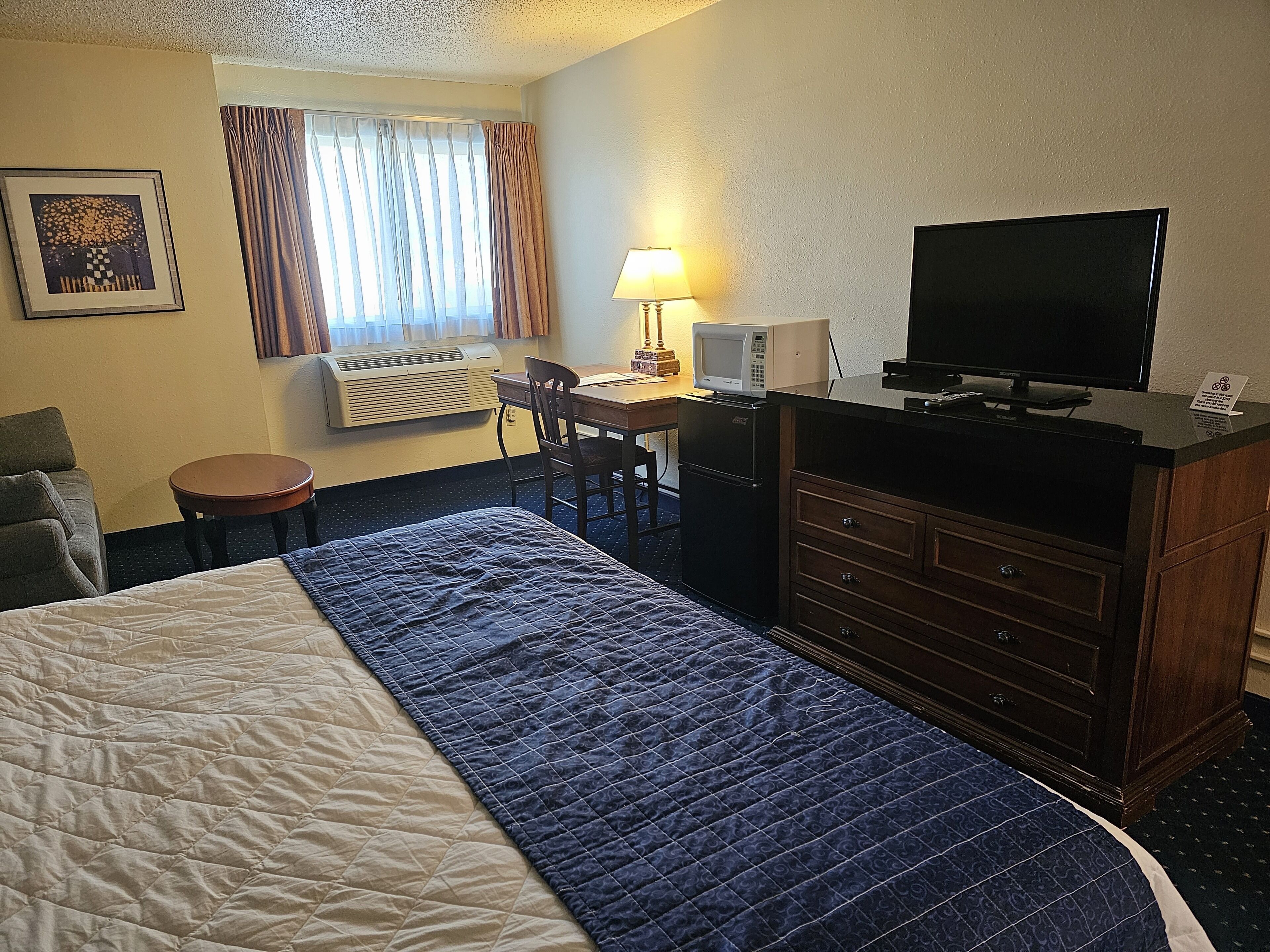 A hotel room with a bed, desk, chair, television, and a small table.