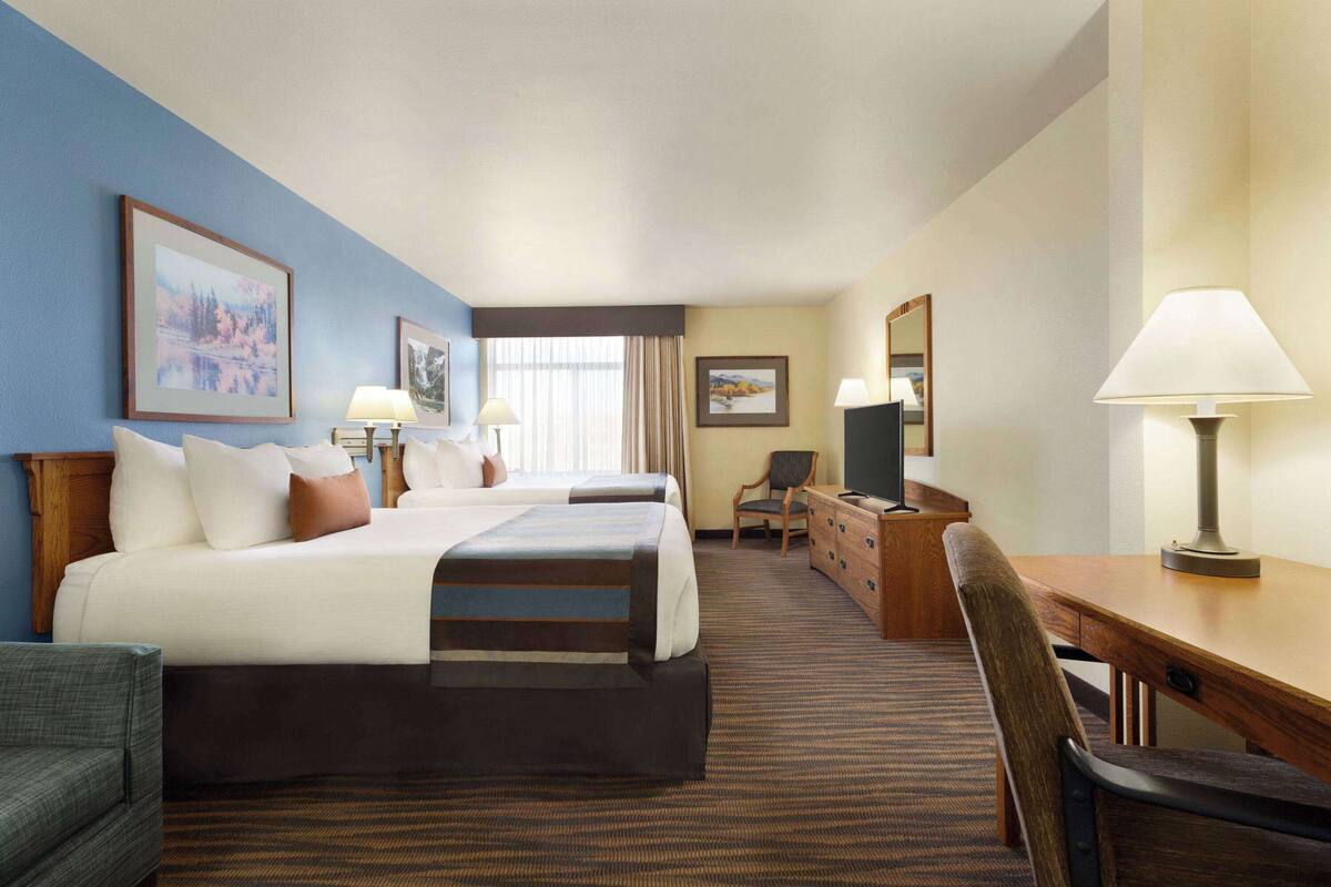 A hotel room with two beds, a desk, a chair, a dresser, and a window with curtains.