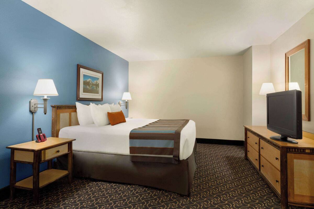 A hotel room with a bed, bedside tables, a television, and a framed picture on the wall.