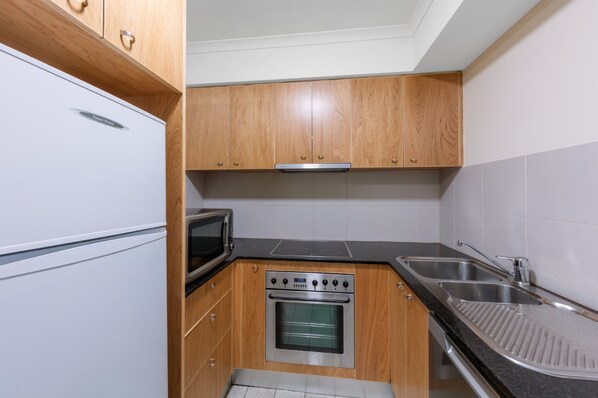 A compact kitchen with wooden cabinets, a built-in oven, a microwave, and a sink.