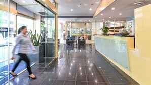 Een moderne hotellobby met een glazen entree, een receptiebalie en een zithoek.