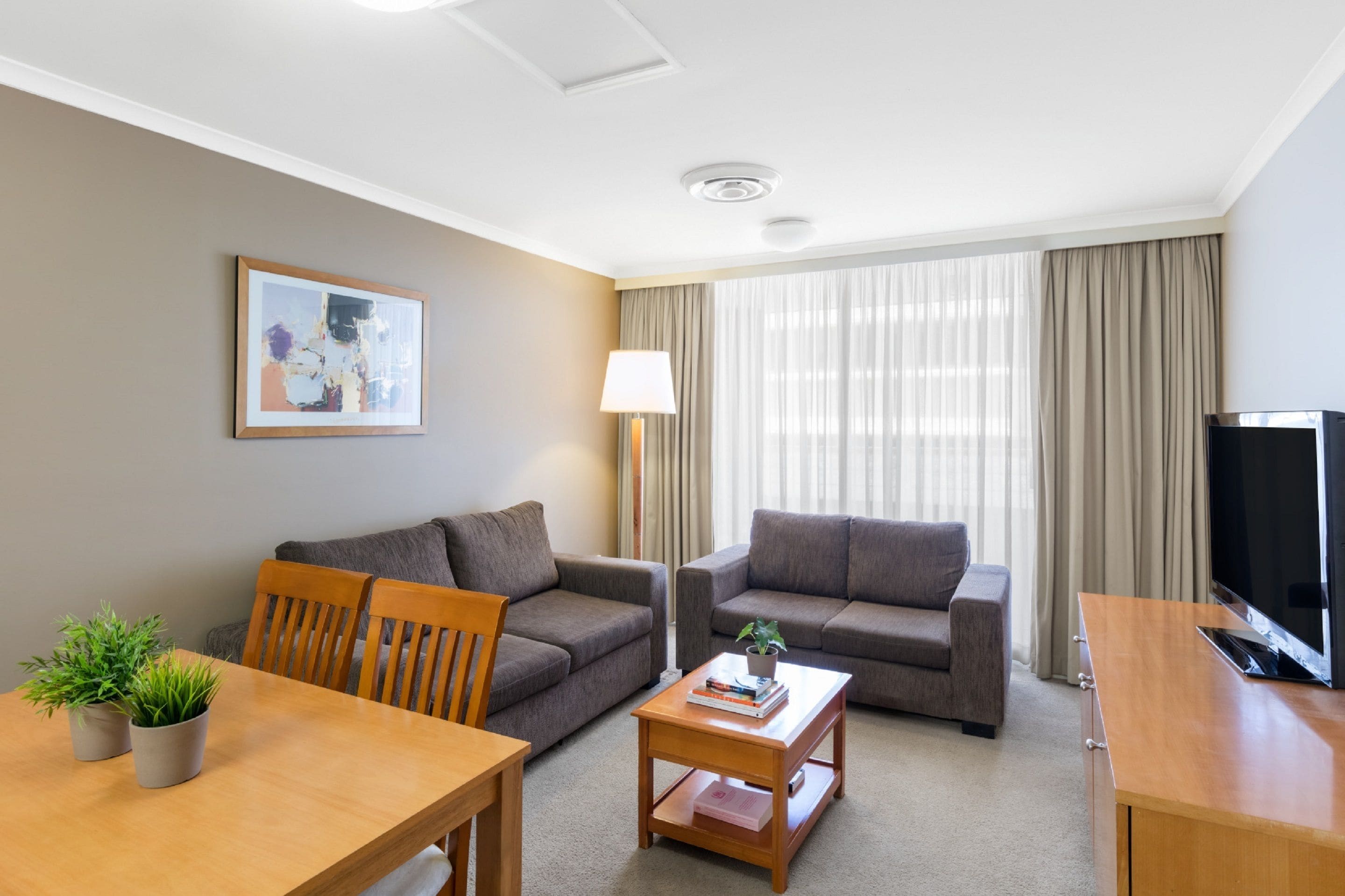 Una habitación de hotel moderna con dos sofás, una mesa de comedor con sillas, un televisor y una lámpara.