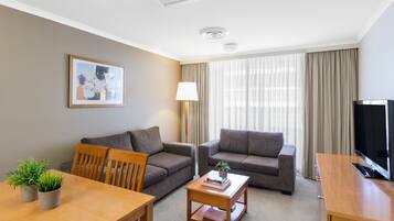 Una habitación de hotel moderna con dos sofás, una mesa de comedor con sillas, un televisor y una lámpara.