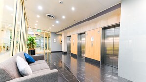 Een moderne lobby met een grijze bank, een potplant en twee liften.