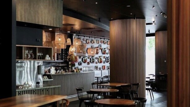 Een modern restaurantinterieur met een bar, houten tafels en hangende verlichtingsarmaturen.