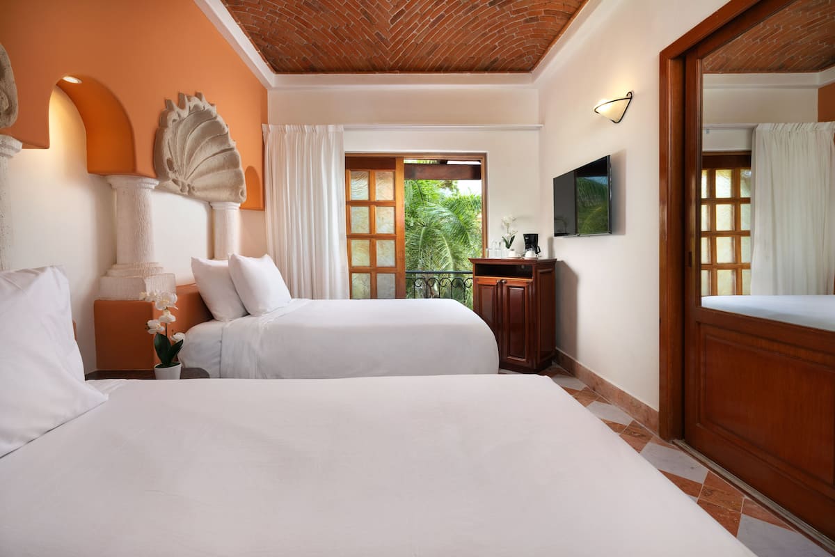 Habitación de hotel con dos camas, un ventanal con vistas a zonas verdes, techo de madera y televisor de pantalla plana en la pared.
